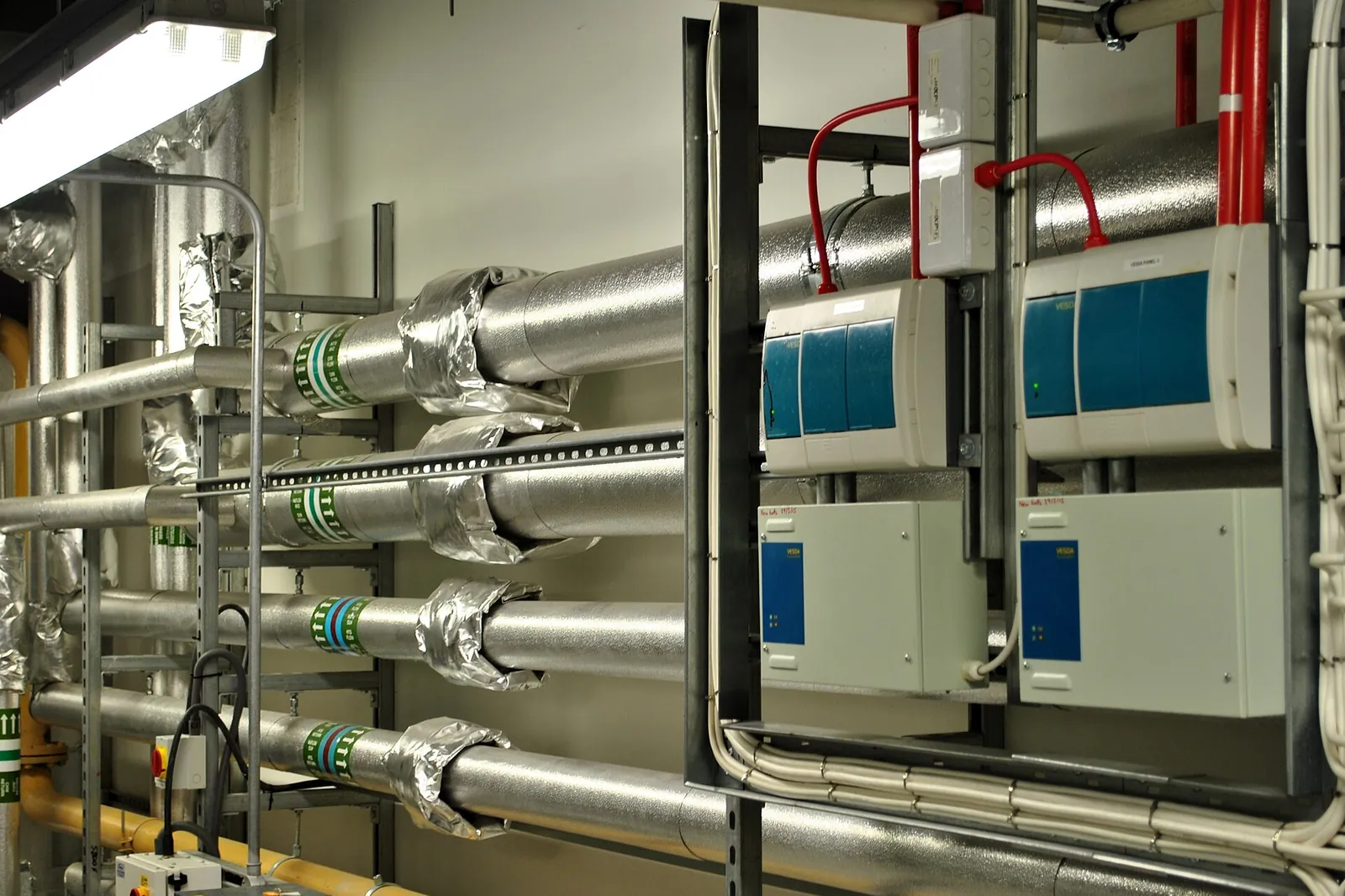 Plant room with insulated pipework, valves and electronic control cabinets mounted on the wall